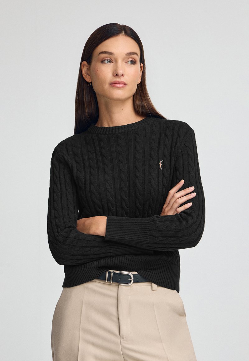 Svart kabelstickad tröja med rund halsringning och långa ärmar. Har ribbat inlägg i nederkant och vid ärmsluten. Logotypdetalj på bröstet.