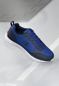 Blue athletic shoe with a smooth synthetic upper, lace-up design, and a white rubber sole. Features a logo on the side and padded collar.
