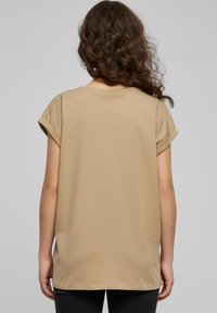Beige t-shirt i bomull med uppvikta korta ärmar, rund halsringning och avslappnad passform. Slät textur, medellång och med rak nederkant.