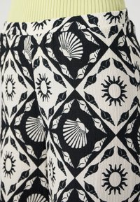 Fekete-fehér mintázatú textil, kagyló és napmotívumokkal, római elrendezésben; a textúrált szövet mélységet és vizuális érdeklődést kölcsönöz.