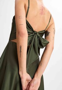 Olive green dress with a large bow detail at the back, featuring thin straps and a smooth, satin-like texture.