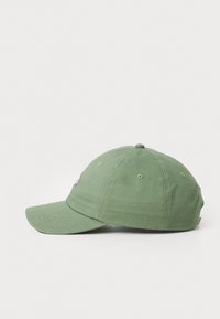Green cotton baseball cap with a curved brim, stitched eyelets, and a logo patch on the front. Smooth texture and casual design.