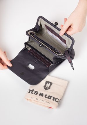 Portafoglio in pelle blu navy con scomparti interni e una fodera a strisce. Una borsa di stoffa con logo è visibile sotto il portafoglio. Chiusura con bottone automatico.