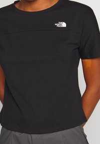 Musta lyhythihainen t-paita, joka on valmistettu pehmeästä kankaasta. T-paidassa on pyöreä kaula-aukko ja vasemmassa ylärinnassa Valkoisen The North Face -logon.