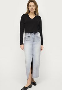 Black v-neck sweater paired with a light blue denim maxi skirt featuring a front slit. Outfit complemented by black flats.