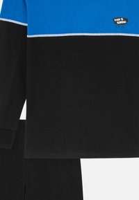 Long-sleeve top in blue and black, featuring a graphic "EASY IS BORING." Textured cotton with contrasting stitching. Paired with black bottoms.