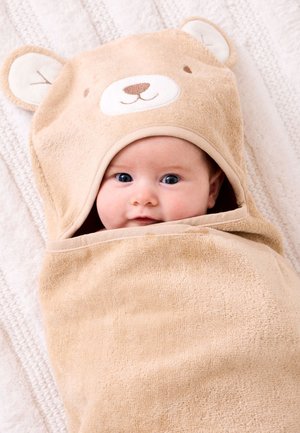 Baby in beigem Kapuzenhandtuch mit Bärengesicht und Ohren eingewickelt, liegend auf einer strukturierten weißen Decke.