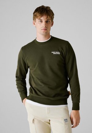 Olijfgroen sweatshirt met lange mouwen, ronde hals en het "RED BULL RACING" logo in het wit. Licht textuur en geribbelde manchetten en onderkant.