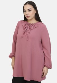 Top lungo rosa a maniche lunghe con colletto arricciato e fiocco, polsini elasticizzati e tessuto testurizzato, progettato con una vestibilità ampia.