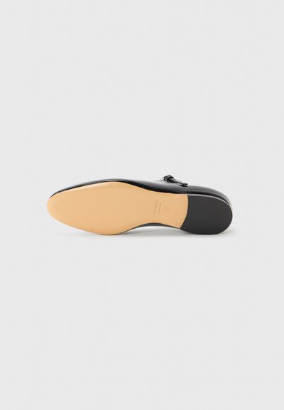 Semelle en cuir noir de forme arrondie, talon en caoutchouc et finition beige. Présente une texture lisse et un marquage subtil sur le côté.