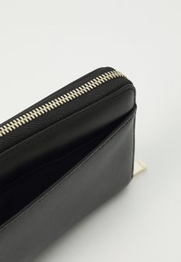Zwart leren portemonnee met een textuur oppervlak, gouden ritssluiting en een gladde binnenzijde. Heeft een minimalistisch ontwerp met een zijtab.
