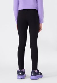 Leggings neri realizzati in un tessuto elastico, design aderente, texture liscia, abbinati a sneakers viola e nere con un logo distintivo.