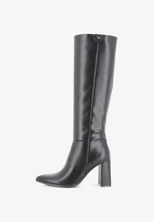 Bota de cuero negra hasta la rodilla con punta afilada y tacón grueso. Textura suave con un ligero brillo. Presenta un acento de logotipo cerca de la parte superior.