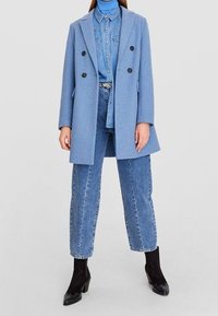 Hellblauer Wollmischung-Doppelkordmantel, getragen über einem Jeanshemd und hochgeschnittenen hellblauen Jeans, kombiniert mit schwarzen Knöchelstiefeln.