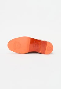 Suela de zapato de cuero marrón con una forma suave y redondeada. Presenta un tacón de goma naranja vibrante y detalles de logotipo grabados. Acabado plano y pulido.