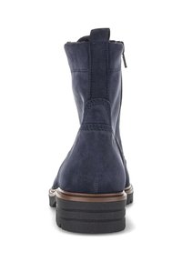 Stivaletti alla caviglia in suede blu navy con zip laterale, suola in gomma spessa e dettagli marroni, visti dal retro su uno sfondo bianco.