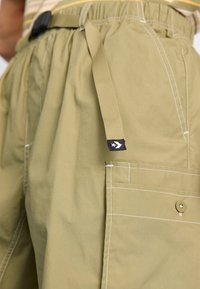 Bermudas cargo en color verde oliva con cintura elástica, correa ajustable, costuras blancas y detalles de bolsillos laterales. Tejido liviano.