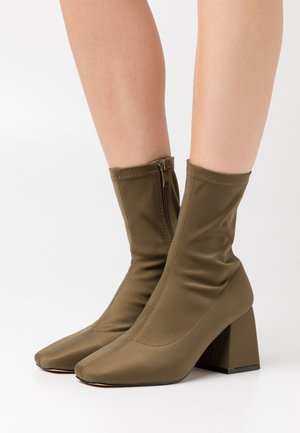 Olivgrüne kurze Stiefel aus glattem Stoff mit spitzen Zehen, Blockabsätzen und einem seitlichen Reißverschluss zum Schließen und Anpassen.