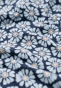 Granatowa tkanina w kwiatowy wzór z białymi stokrotkami i czerwonymi akcentami. Miękka faktura i pomarszczony wygląd.