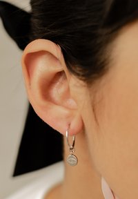 Orecchino a cerchio in argento con un piccolo ciondolo rotondo texturizzato pendente. Vista ravvicinata dell'orecchino su un orecchio umano.