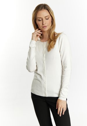 Cardigan bianco a maniche lunghe con scollo rotondo e chiusura frontale con bottoni. Tessuto morbido e leggero con una texture liscia, forma aderente.