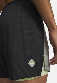 Mustad sportlühikesed püksid tekstuurse, perfoteeritud mustriga. Omavad heledat halli paneeli ja rohelise logoga aksenti.