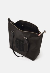 Black nylon tote bag with gold zipper, two shoulder straps, and a prominent black logo on the front. Interior includes pockets and lining.