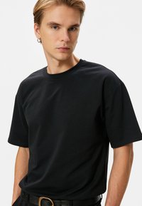 Mustat puuvillapaidat, joissa on lyhyet hihat, klassinen pyöreä kaula-aukko ja rento istuvuus. Sileä rakenne, ei näkyviä kuvioita tai koristeita.