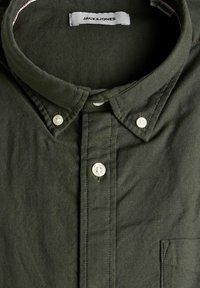 Chemise boutonnée vert foncé avec des boutons blancs et un col boutonné, avec une étiquette "JACK & JONES" visible à l'intérieur du col.