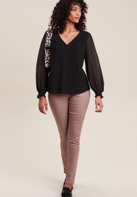 Blouse noire à manches longues en gaze et décolleté en V, accompagnée de pantalons beiges bien ajustés. Les accessoires comprennent un sac à main en imprimé léopard et un collier en argent.