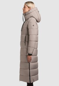 Lang, fyldig jakke i lys grå med hætte, der har en lynlåslomme på siden og justerbare snore. Glat tekstur, quiltet design.