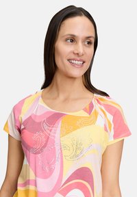 Kolorowy t-shirt z krótkim rękawem z miękkiego materiału, z wzorem w wir w kolorach różowym, żółtym i białym, ozdobiony akcentami z cyrkonii na klatce piersiowej.