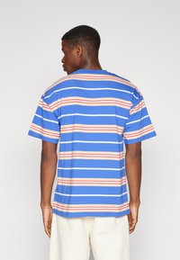 Camiseta de manga corta azul con rayas horizontales en rojo, azul claro y beige. Material de algodón, corte holgado, escote redondo.