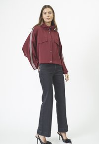 Burgundy cropped takki, jossa on kaksi etutaskua, nappisulku ja valkoiset raidat hihoissa. Yhdistetty tummaihoisiin farkkuihin ja mustiin korkokenkiin.