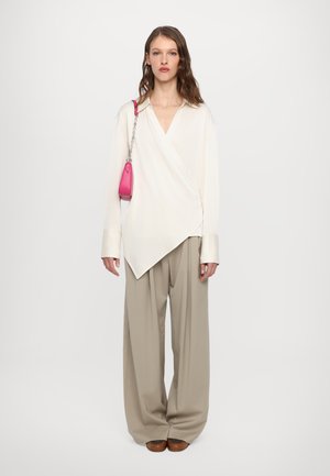 Blusa bianca avvolgente con scollatura a V e maniche lunghe, abbinata a pantaloni a gamba larga beige chiaro. Accessorio: borsa piccola rosa con tracolla a catena.
