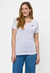 Hvit bomull t-skjorte med rund hals og korte ermer, med en liten marineblå logo på brystet. Kombinert med blå denimbukser.