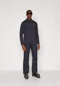 Tengerészkék hosszú ujjú cipzáros felső és hozzáillő nadrág szintetikus anyagból, logó díszítéssel és cipzáras zseb részlettel. Fekete síbakancsok tartoznak hozzá.