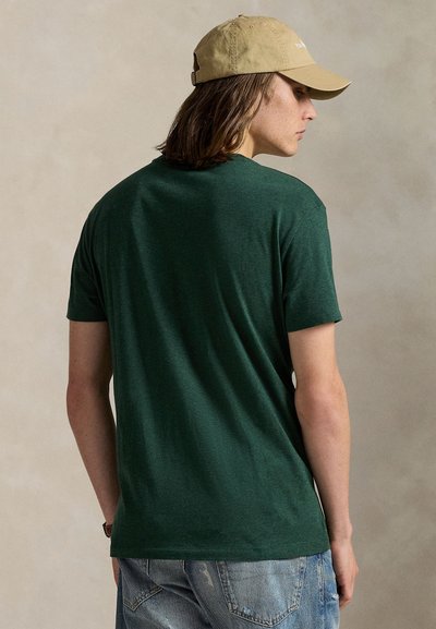 Σκούρο πράσινο βαμβακερό κοντομάνικο μπλουζάκι με ανοιχτή εφαρμογή και στρογγυλή λαιμόκοψη. Φορεμένο με ανοιχτό μπ�εζ καπέλο που έχει απλό σχέδιο.