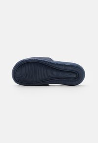 Sötétkék, slip-on stílusú cipő, texturált gumitalppal, sima felsőrésszel és hangsúlyos talpmintázattal a tapadásért.
