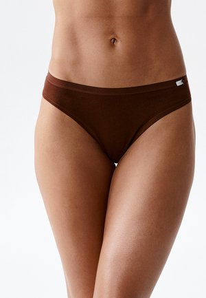 Damski tułów w brązowej bawełnianej bieliźnie bikini na jednolitym białym tle.