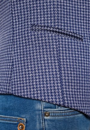 Granatowa marynarka w wzory z teksturowanym wzorem w zębatkę, z kieszenią z przodu, zestawiona z jasnoniebieskimi dżinsami.