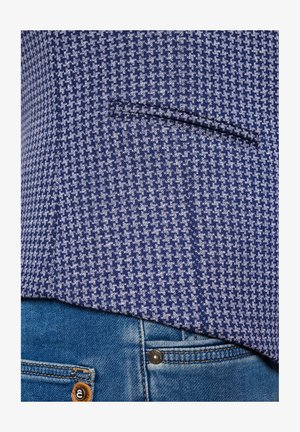 Granatowa marynarka w wzory z teksturowanym wzorem w zębatkę, z kieszenią z przodu, zestawiona z jasnoniebieskimi dżinsami.