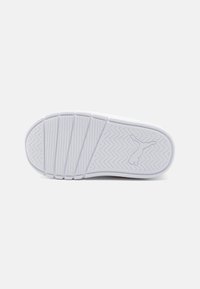 Semelle de sneaker blanche avec un motif en chevrons, présentant un logo en relief et des zones de préhension texturées. Fini lisse avec des sections en caoutchouc segmentées.