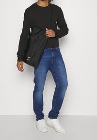 Musta pitkähihainen paita, siniset farkut ja valkoiset tennarit. Musta olkalaukku roikkuu olkapäällä, siinä on yksinkertainen muotoilu.