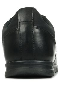 Scarpe da ginnastica nere con una parte superiore in pelle liscia, dettagli in nylon testurizzato e suola in gomma, riprese dalla vista posteriore.