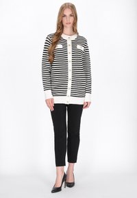 Cardigan cu dungi alb-negru, cu nasturi în față, decolteu rotund și manșete albe în contrast. O pereche de pantaloni negri adaptați și tocuri.