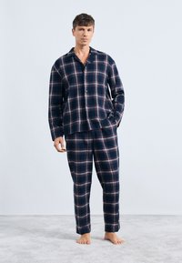 Conjunto de pijama de cuadros marino que incluye una camisa de botones y pantalones a juego, con mangas largas, tejido suave y un corte relajado.