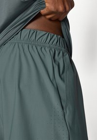 Αθλητικά σορτς ανδρών σε σκούρο τιρκουάζ, κατασκευασμένα από �απαλό, ελαφρύ ύφασμα. Διαθέτουν ελαστική μέση και τρύπες στην πλευρά.