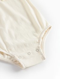 Baumwoll-Bodysuit in Off-White, mit kurzen Ärmeln, Druckknöpfen am Boden und gerafften Kanten für eine enganliegende Passform.