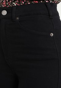 Jeans in denim nero caratterizzati da un design attillato, stile classico a cinque tasche e dettagli in metallo argentato sulla cintura e sulle tasche.